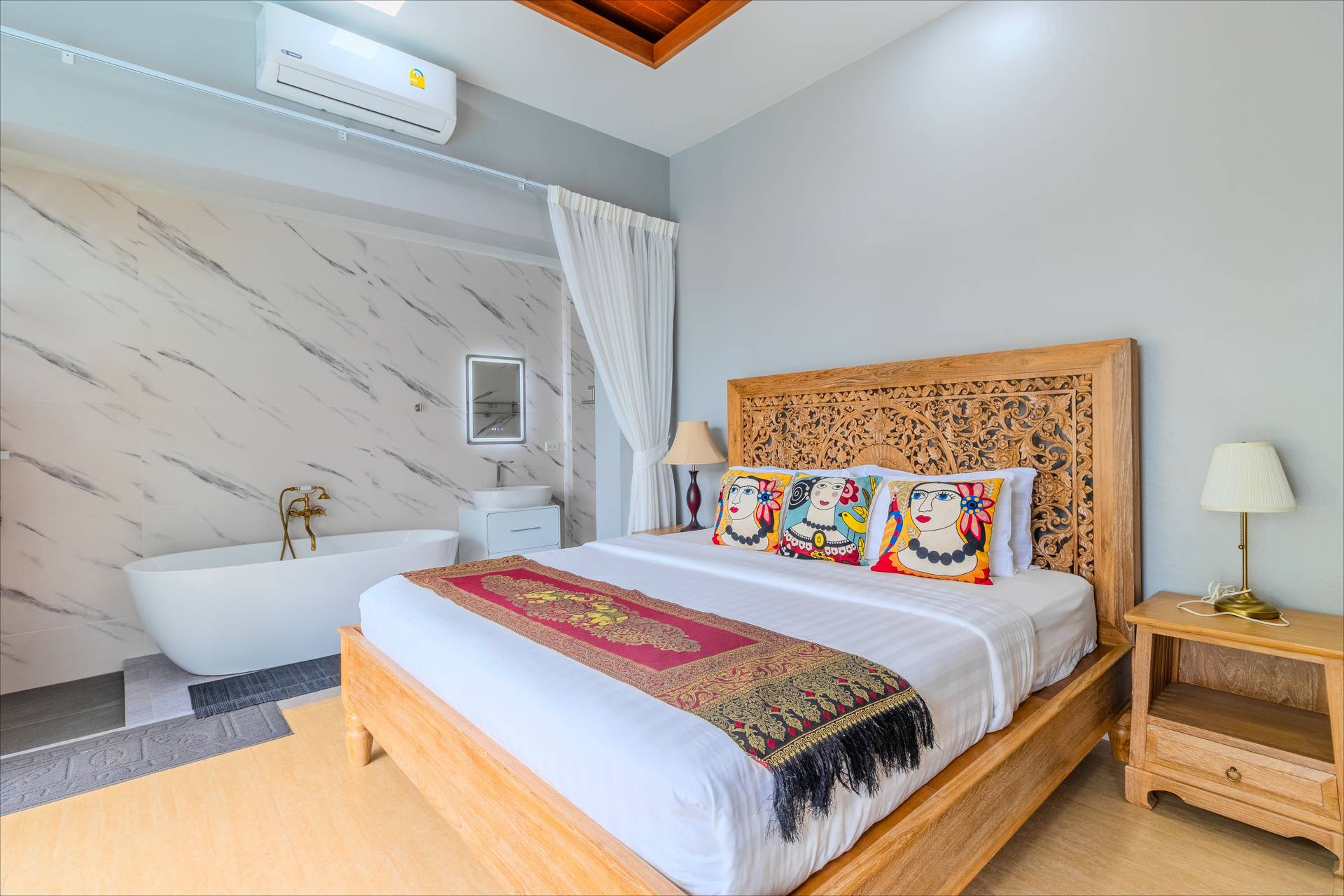 Elegant bedroom with carved teak headboard and freestanding bathtub