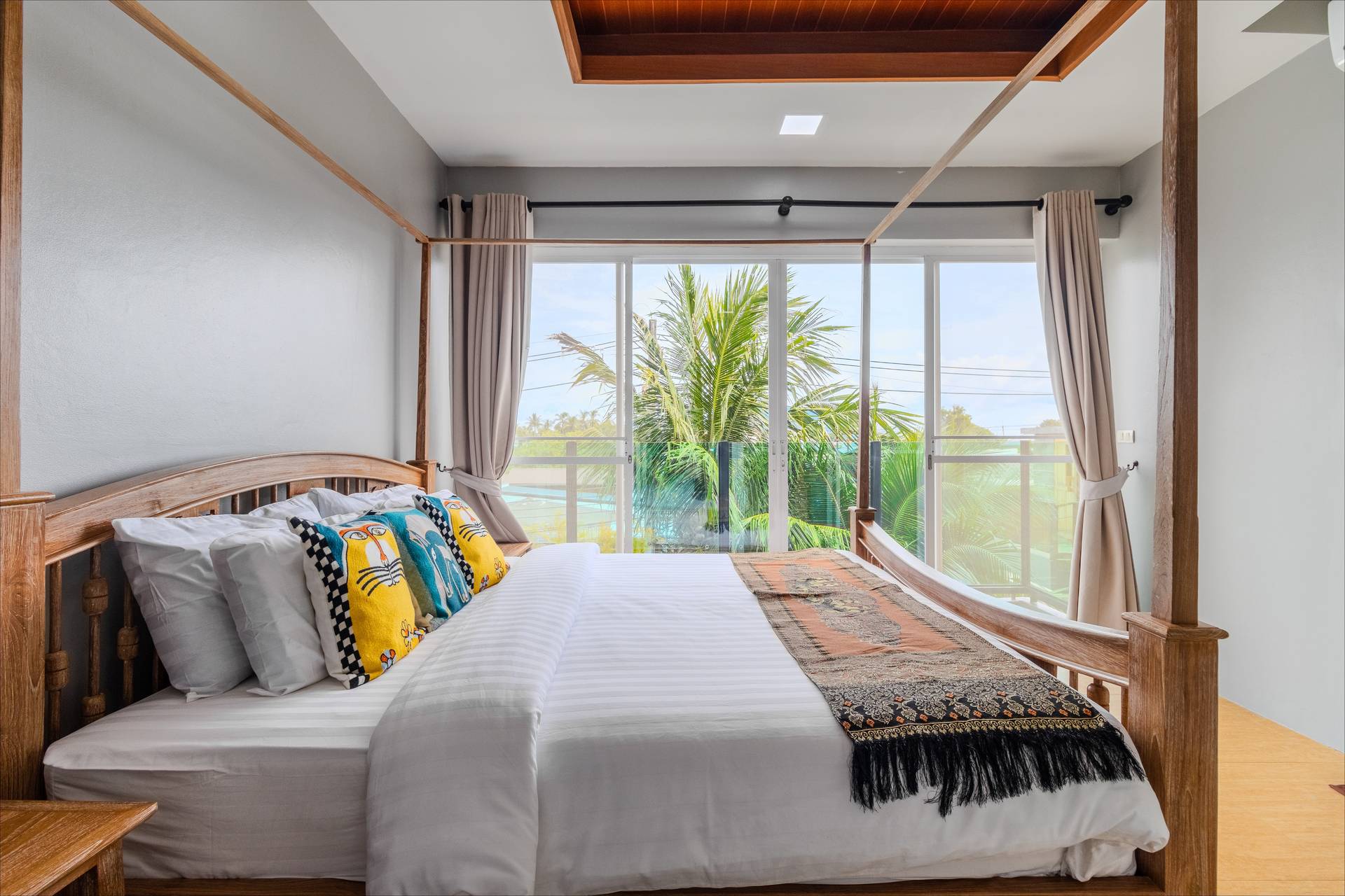 Bright four-poster bedroom with tropical garden views and art cushions