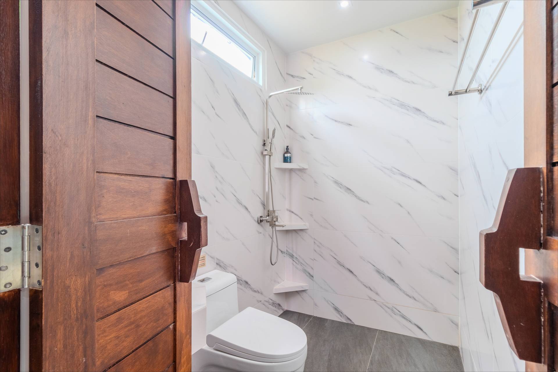 Marble-tiled walk-in shower with rain head and teak wood doors