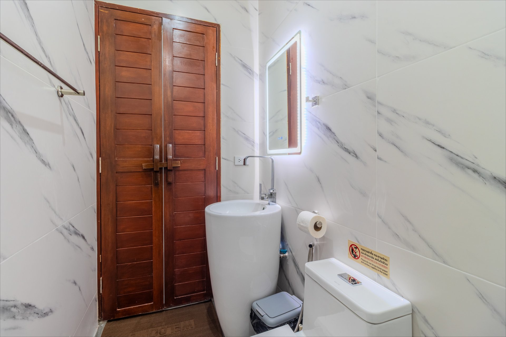 Modern marble-walled bathroom with LED-lit mirror and pedestal basin