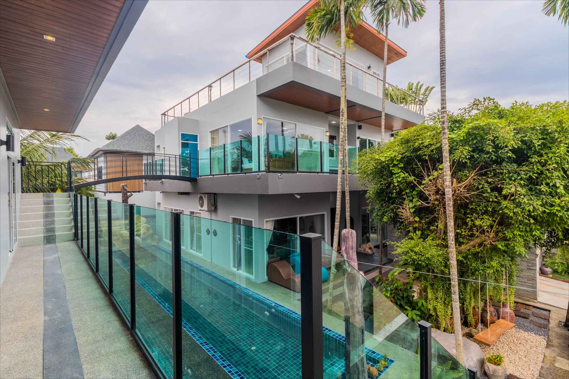 Multi-level exterior with turquoise glass-walled pool and lush landscaping
