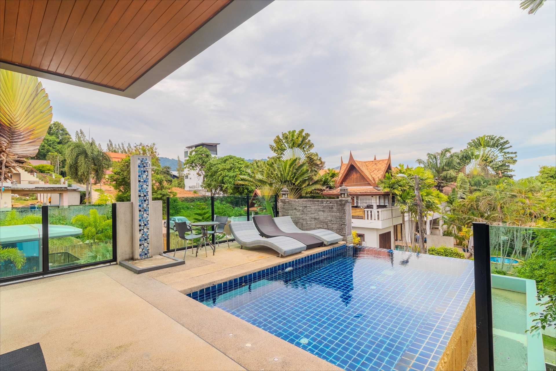 Rooftop infinity pool with outdoor shower and panoramic Rawai hillside views at dusk