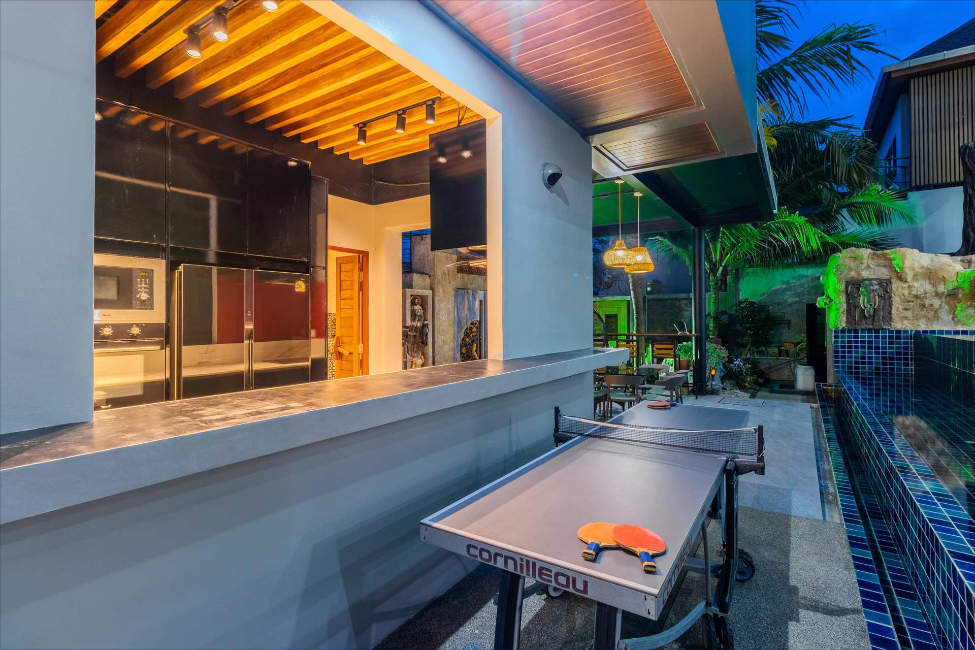 Blue-tiled rooftop pool illuminated at twilight with tropical surroundings